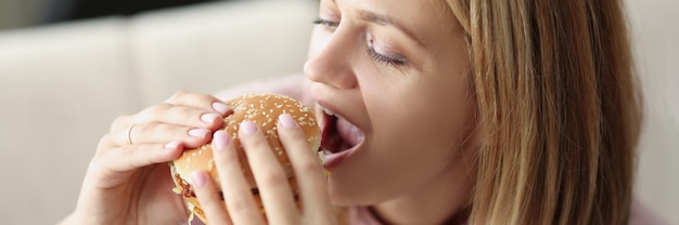 Młoda kobieta je pysznego, apetycznego hamburgera w domu