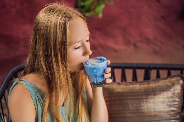 Młoda Kobieta Je śródziemnomorskie śniadanie Siedząc Przy Kanapie I Pije Modny Napój Niebieska Latte Gorący Latte Z Groszkiem Motylkowym Lub Niebieska Spirulina Latte