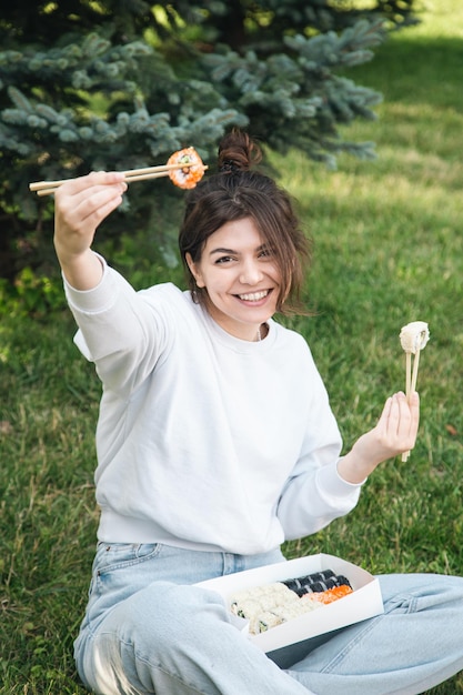 Młoda kobieta je sushi na pikniku w parku w naturze