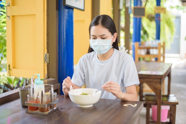 Młoda kobieta je tajskie jedzenie uliczne, ubrana w maskę, nowa koncepcja normalnego jedzenia