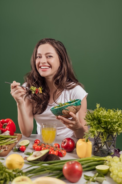 Młoda kobieta je zdrowe jedzenie siedząc w pięknym wnętrzu z zieloną ścianą w tle