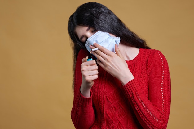 Młoda kobieta jest ubranym medyczną ochronną maskę i trzyma papieros w jej usta przez maski