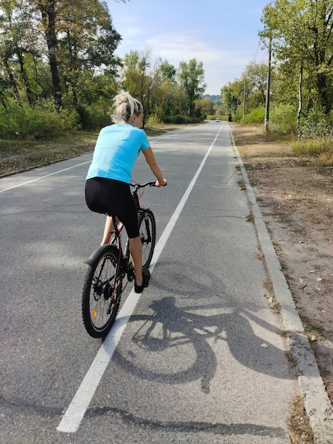 Młoda kobieta jeździ rowerem wzdłuż asfaltowej drogi w parku Aktywna rekreacja w przyrodzie