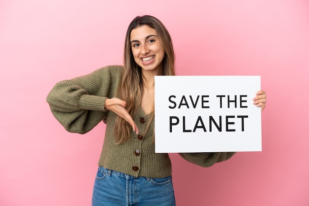 Młoda kobieta kaukaska na białym tle na różowym tle trzymając tabliczkę z tekstem Save the Planet i wskazując ją