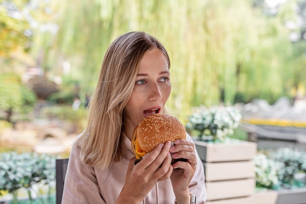 Młoda Kobieta Kaukaski Jedzenie Cheeseburgera W Kawiarni Na świeżym Powietrzu W Lecie.