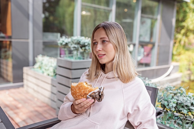Zdjęcie młoda kobieta kaukaski jedzenie cheeseburgera w kawiarni na świeżym powietrzu w lecie.