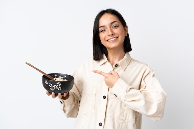 Młoda kobieta kaukaski na białym tle na białej ścianie i wskazując go, trzymając miskę makaronu pałeczkami
