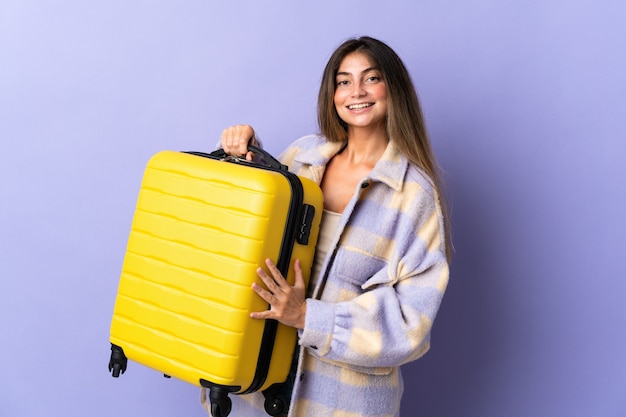 Młoda kobieta kaukaski na fioletowym tle na wakacjach z walizką podróżną
