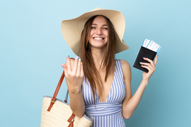 Młoda kobieta kaukaski w letnie wakacje trzymając paszport na białym tle na niebieskim tle, zapraszając z ręką. Cieszę się, że przyszedłeś