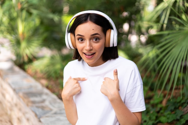Młoda kobieta kaukaski ze słuchawkami na zewnątrz z wyrazem twarzy zaskoczenia