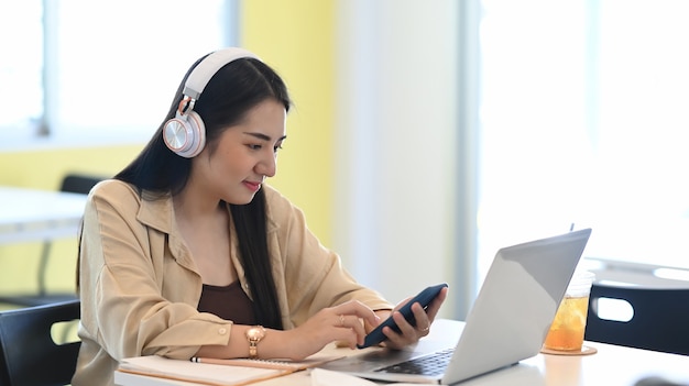 Młoda kobieta kolegium studia online z komputera przenośnego i przy użyciu telefonu mart siedząc w kawiarni.