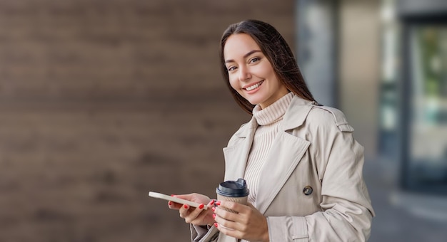 Młoda kobieta korzysta z telefonu komórkowego, uśmiecha się i odwraca wzrok na tle biurowca na ulicy