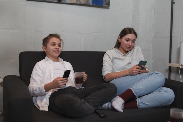 Młoda kobieta korzysta ze smartfona, podczas gdy jej syn ogląda telewizję