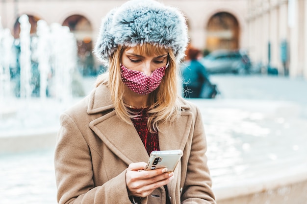 Młoda Kobieta Korzystająca Z Funkcji śledzenia Telefonu Komórkowego Rozprzestrzenianie Się Koronawirusa - Nowa Koncepcja Normalnego Stylu życia Z Dziewczyną Z Pokolenia Tysiąclecia Noszącą Maskę Na Twarzy Oglądającą Inteligentny Telefon Komórkowy.