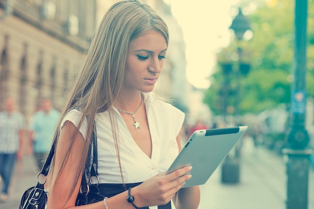 Młoda kobieta korzystająca z tabletu cyfrowego stojąca na ulicy