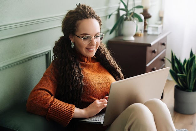 Młoda kobieta korzystających z zakupów online i e-learningu na laptopie w domu Zakupy w domu i e-learning z szczęśliwą kobietą za pomocą laptopa na kanapie