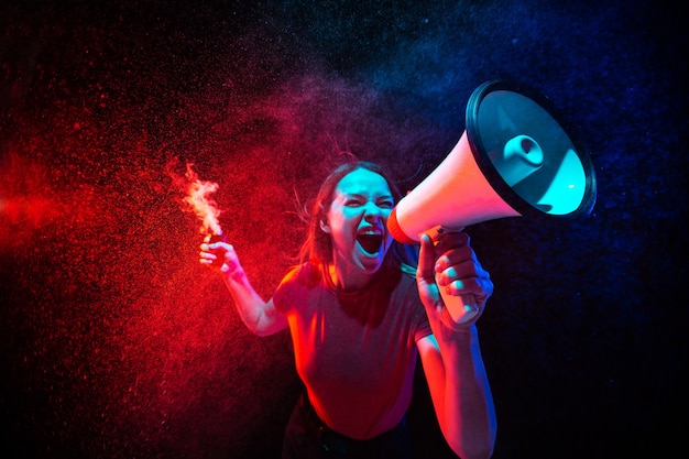 Młoda kobieta krzyczy z megafonem i dymem w neonowym świetle na czarnym tle
