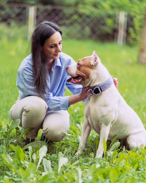 Młoda Kobieta Kucająca I Pieszcząca Amerykański Pitbull Terrier W Parku Szczęśliwy Pies Z Wystawionym Językiem