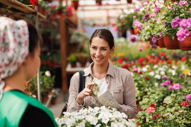 Młoda kobieta kupuje kwiaty doniczkowe od młodej kobiety-przedsiębiorcy w centrum ogrodniczym.