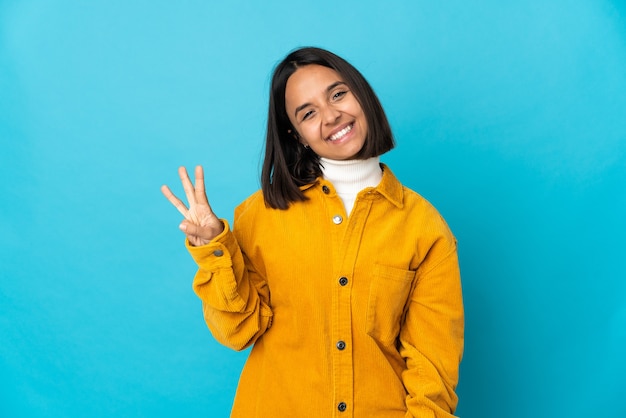 Młoda kobieta Łacińskiej na białym tle na niebieskiej ścianie szczęśliwa i licząc trzy palcami