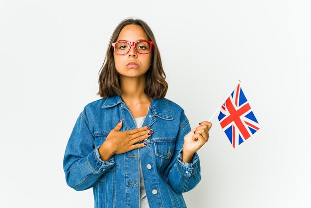 Młoda kobieta Łacińskiej trzymającej angielską flagę na białym tle, składając przysięgę, kładąc rękę na piersi.
