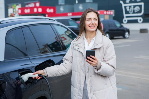 Zdjęcie młoda kobieta ładuje swój samochód elektryczny na stacji ładowania w mieście koncepcja paliwa ekologicznego