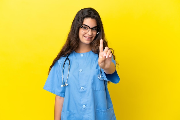 Młoda kobieta lekarz chirurg odizolowana na żółtym tle pokazując i podnosząc palec