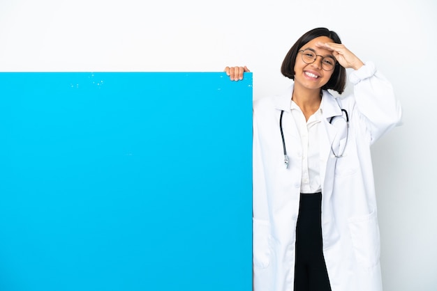 Młoda kobieta lekarz rasy mieszanej z dużym plakatem na białym tle salutowanie ręką z happy wypowiedzi