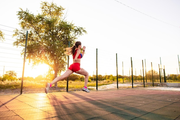 Zdjęcie młoda kobieta lekkoatletka z amputowanym ramieniem i oparzeniami na ciele biega wokół boiska sportowego ona biegnie krótki dystans na świeżym powietrzu o zachodzie słońca