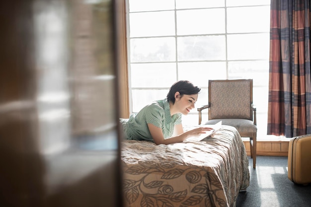 Młoda kobieta leżąca na łóżku w pokoju motelowym przy użyciu cyfrowego ekranu dotykowego tabletu