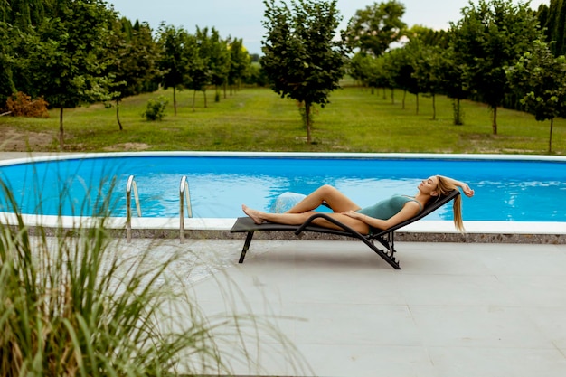 Młoda kobieta leżąca na pokładzie zwęglonym przy basenie na podwórku domu