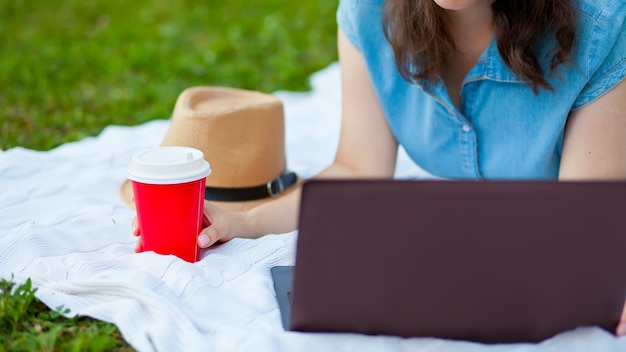 Młoda kobieta leży na kratę i za pomocą laptopa w parku
