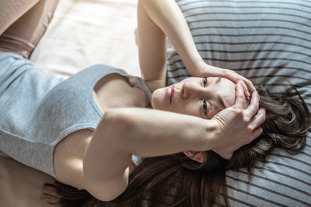 Młoda kobieta leży w łóżku i trzyma się za głowę rękami, doświadcza migreny ból głowy Pojęcie bezsenności spowodowanej stresem, lękiem i problemami