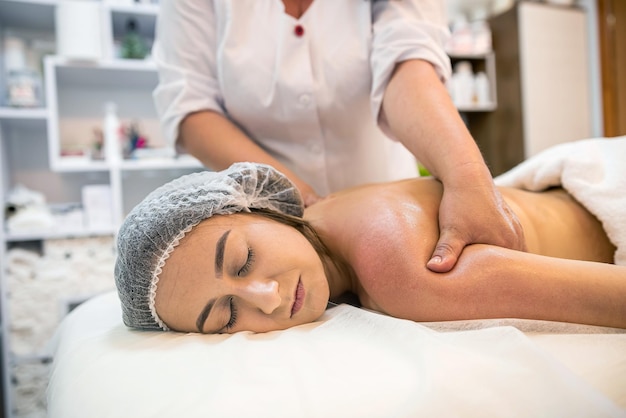 Młoda kobieta leży z zamkniętymi oczami i odpoczywa podczas masażu pleców w salonie piękności Profesjonalna masażystka pracująca ze swoim klientem Piękna dziewczyna ma masaż pleców w spa