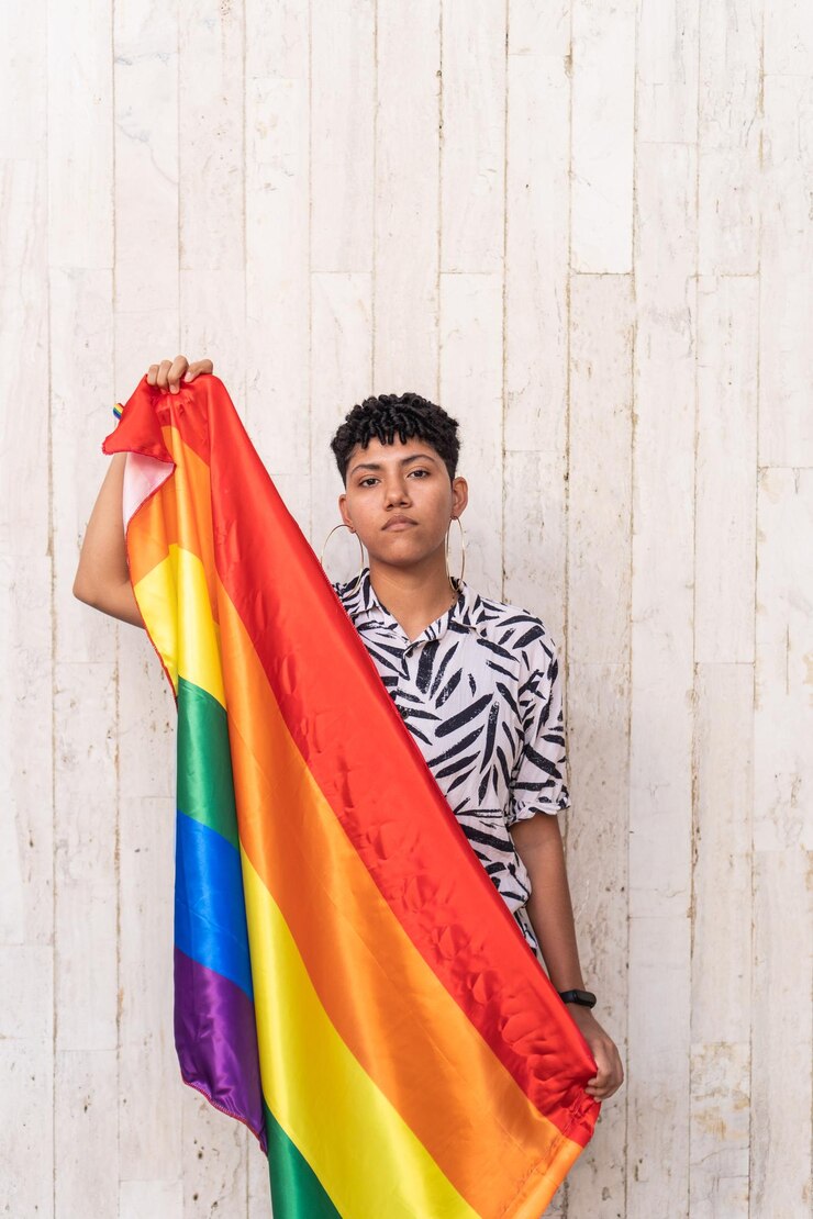 Młoda kobieta LGBT pozuje z tęczową flagą na ulicy