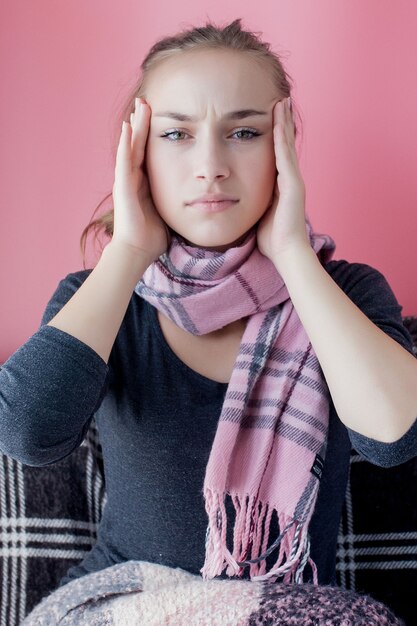 Młoda kobieta ma ból głowy na różowym tle.