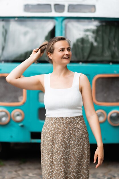 Młoda kobieta ma na sobie białą koszulkę i pozuje na tle starego autobusu
