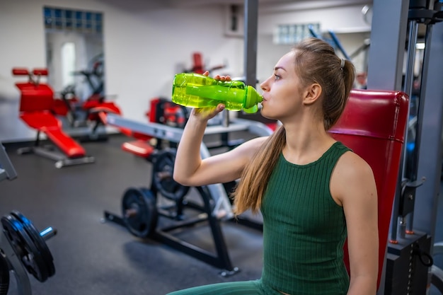 Młoda kobieta ma przerwę po treningu sportowym i wodę pitną z zielonej szklanej butelki Samoobsługowa równowaga życia i koncepcja zdrowego stylu życia