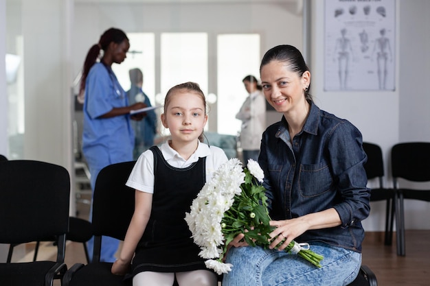 Młoda kobieta, mała dziewczynka patrząca w kamerę, siedząca na kanapach w recepcji kliniki medycznej. Matka, córka niosąca kwiaty do hospitalizowanego krewnego. Członkowie rodziny czekają w holu wieży medycznej.