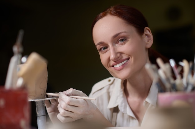 Młoda kobieta malująca ceramikę i wyglądająca na zaangażowaną