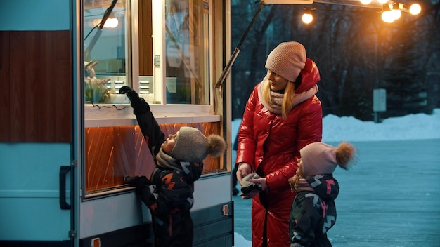 Młoda kobieta, matka z dziećmi, stojąca w pobliżu małego sklepu w pobliżu lodowiska