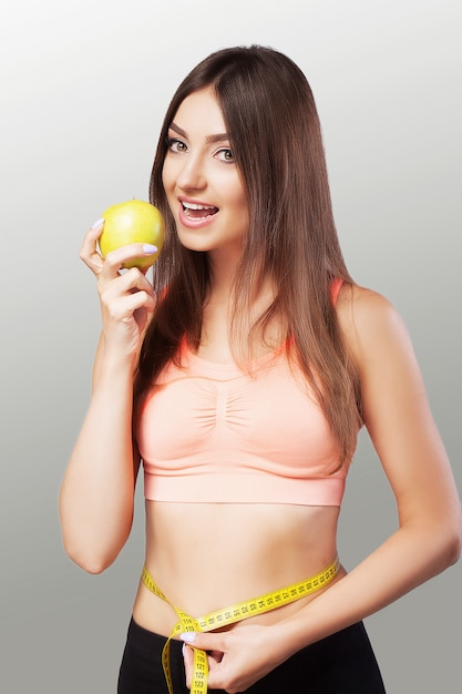 Młoda kobieta mierzy talię taśmą mierniczą i je jabłko. Ścisła dieta. Piękne ciało.