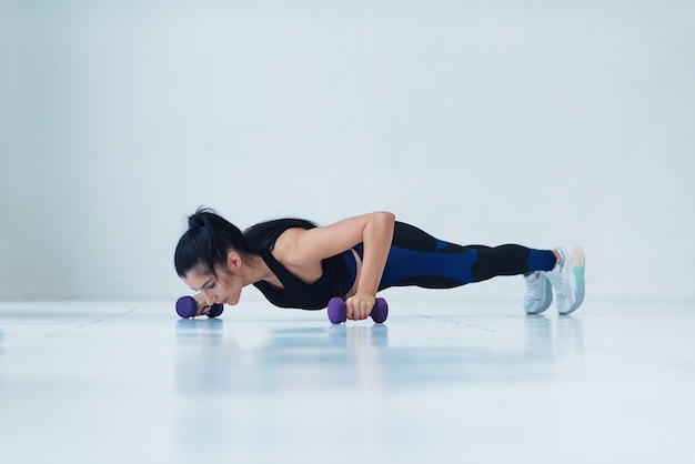 Zdjęcie młoda kobieta mięśni robi pushup ćwiczenia z hantlami na ciężki trening na siłowni