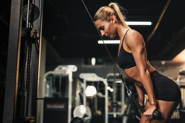 Młoda kobieta mięśni robi trening na maszynie dla jej mięśni ramion na siłowni.