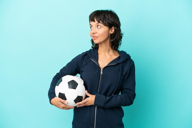 Młoda kobieta mieszanej rasy futbolowej na białym tle na niebieskim tle patrząc z boku