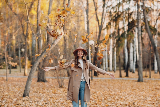 Młoda kobieta model w jesiennym parku z żółtymi liśćmi klonu. Jesienna moda.