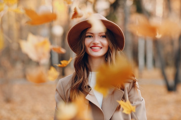 Młoda kobieta model w parku jesień z żółtymi liśćmi klonu. Jesienna moda.