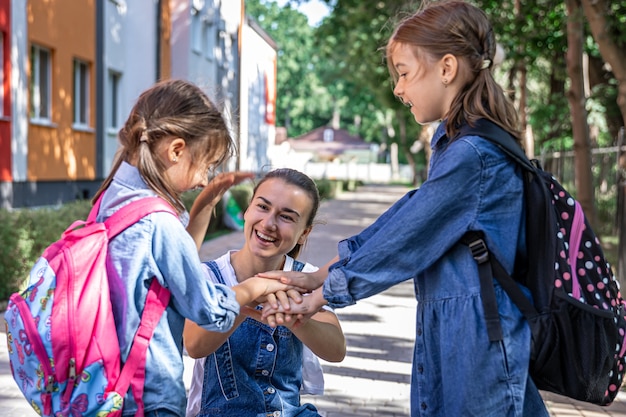 Młoda kobieta moralnie wspiera córki trzymając się za ręce, zachęca dzieci, towarzyszy uczniom do szkoły.