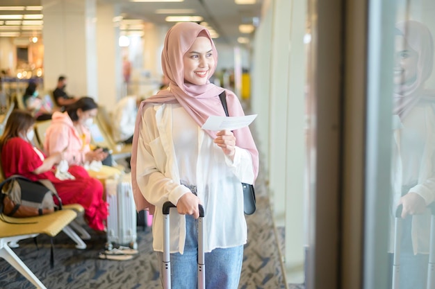 Młoda kobieta muzułmańska podróżniczka niosąca walizki na międzynarodowym lotnisku