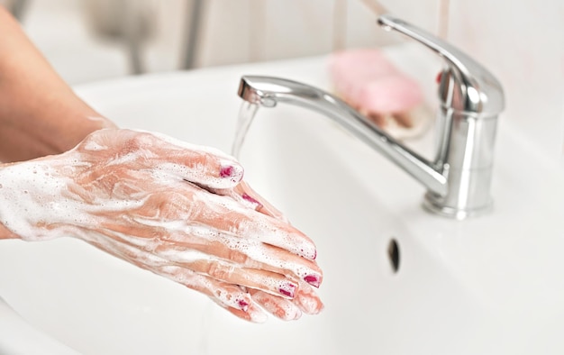Młoda kobieta myje ręce pod kranem z mydłem. Szczegóły na skórze pokrytej mydlinami. Koncepcja higieny osobistej - zapobieganie epidemii koronawirusa covid 19